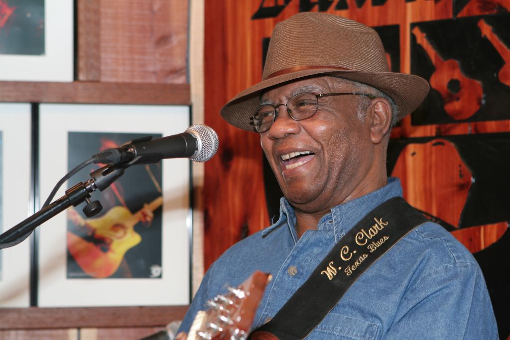 W. C. Clark smiling, singing and playing guitar.