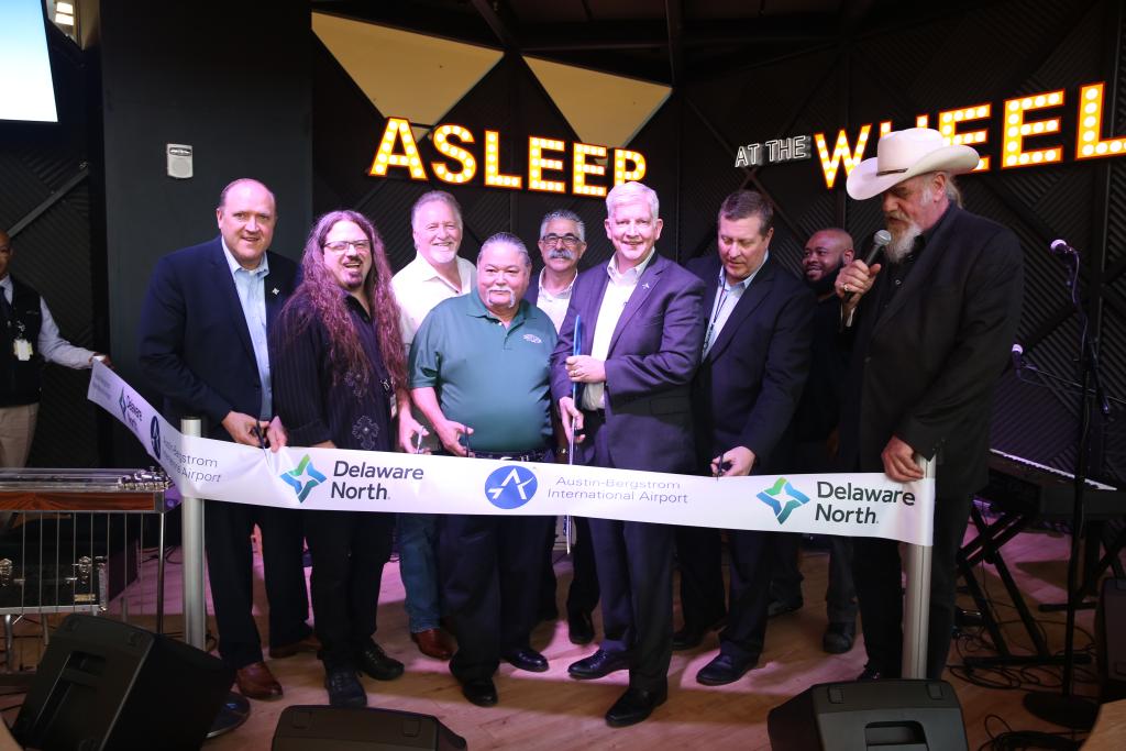 Musicians, AUS, and Delaware North Company staff smile and prepare to cut a ribbon at the Asleep at the Wheel stage.