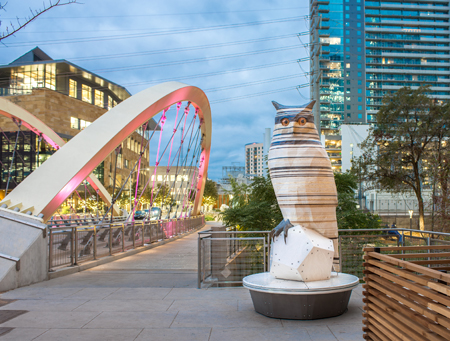 AIPP Kempelen's Owls sculpture near downtown bridge. Ten foot tall owl sculpture with bench for seating near downtown library