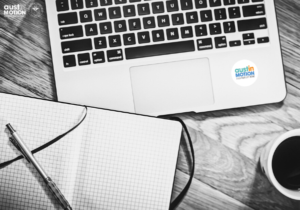 alt='close up black and white photo of a laptop keyboard, cup of coffee, and a notebook with a pen laying over the top'