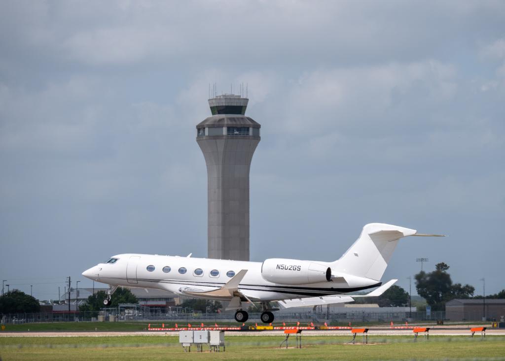 A private jet is departing from AUS with the Air Traffic Control tower in the background.