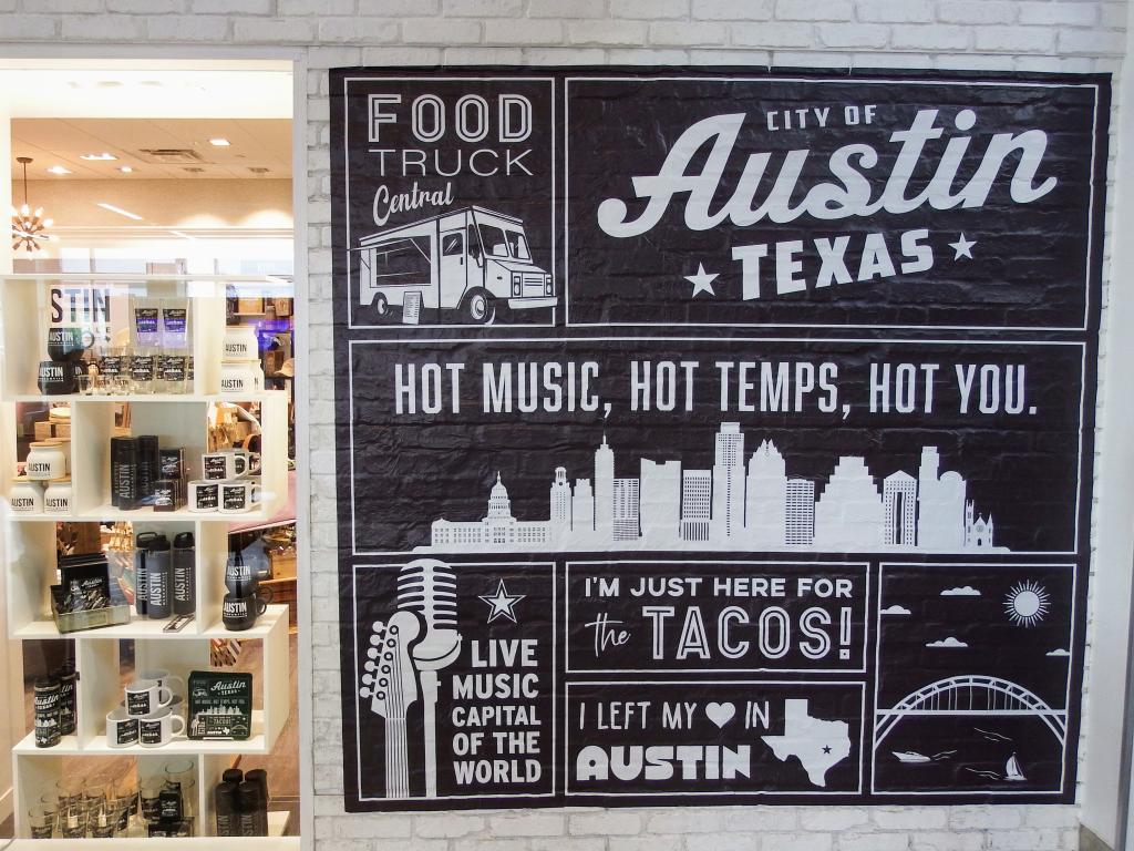Photo of the large sign located outside of Austin Mercantile at AUS. It has different Texas and Austin themes including the quote "Hot music, hot temps, hot you."