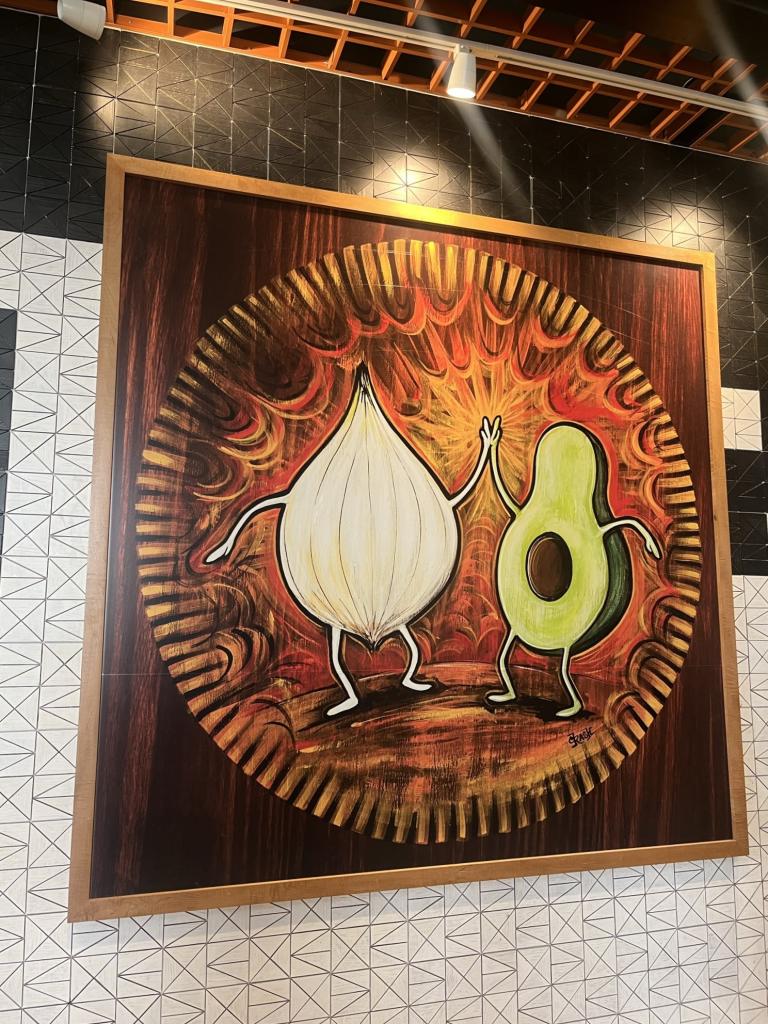 Photo of a large painting on the wall at AUS of an onion and avocado high-fiving.
