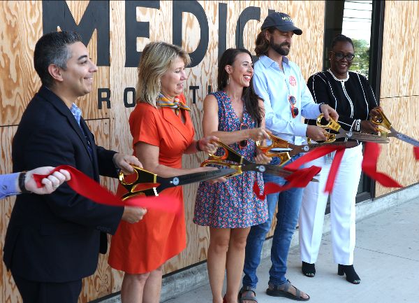 Several people cutting a long ribbon with giant scissors celebrating the opening of a new business