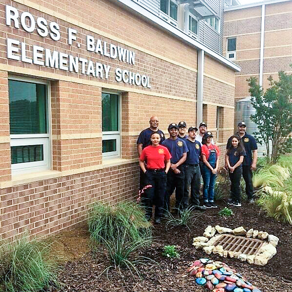 Group photo of firefighters and firefighters-in-training that built a garden at Baldwin Elementary. Photo is taken in the garden area.