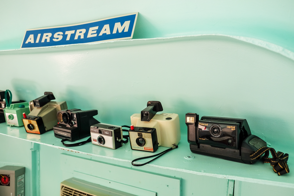 Photo of a teal shelf with several old cameras on it. A sign above reads "Airstream"