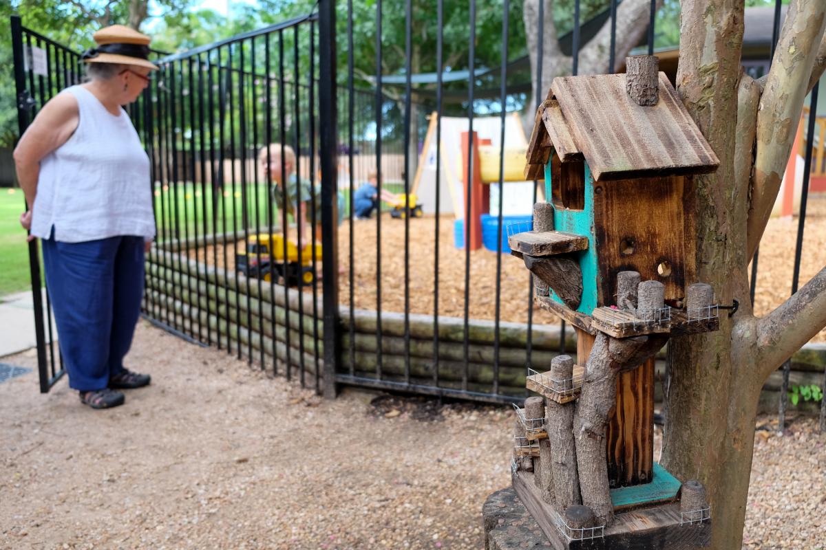 Teacher speaks with student through a black metal gate. In the foreground, there is a multi-tiered bird house.