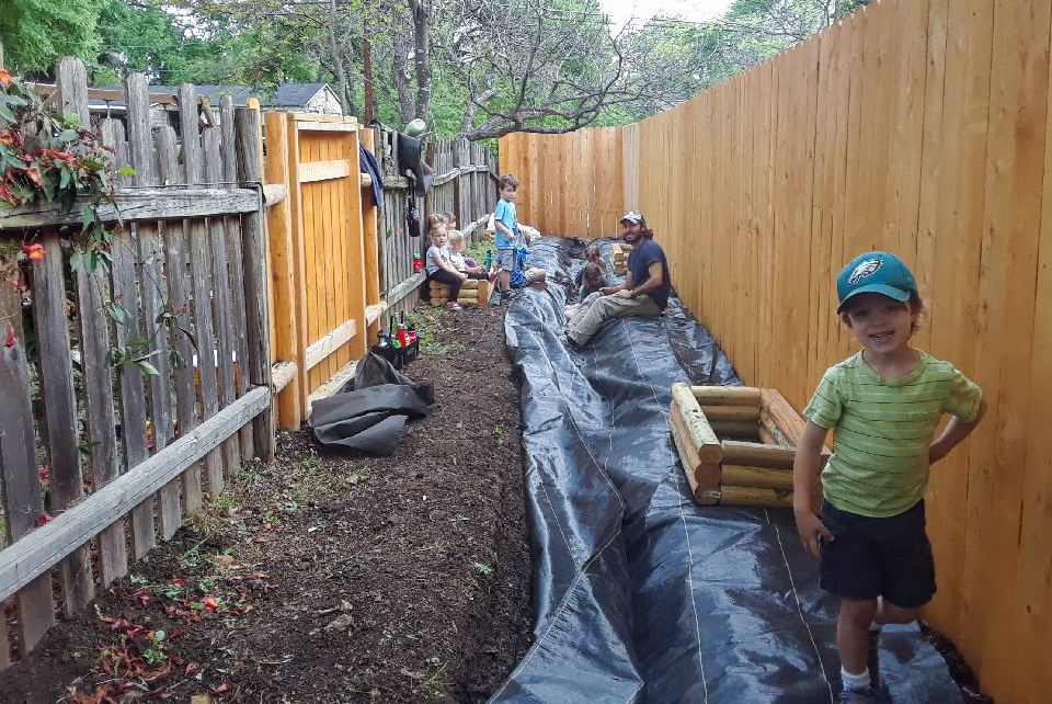 Kids stand in the trench area where they are planting a garden.