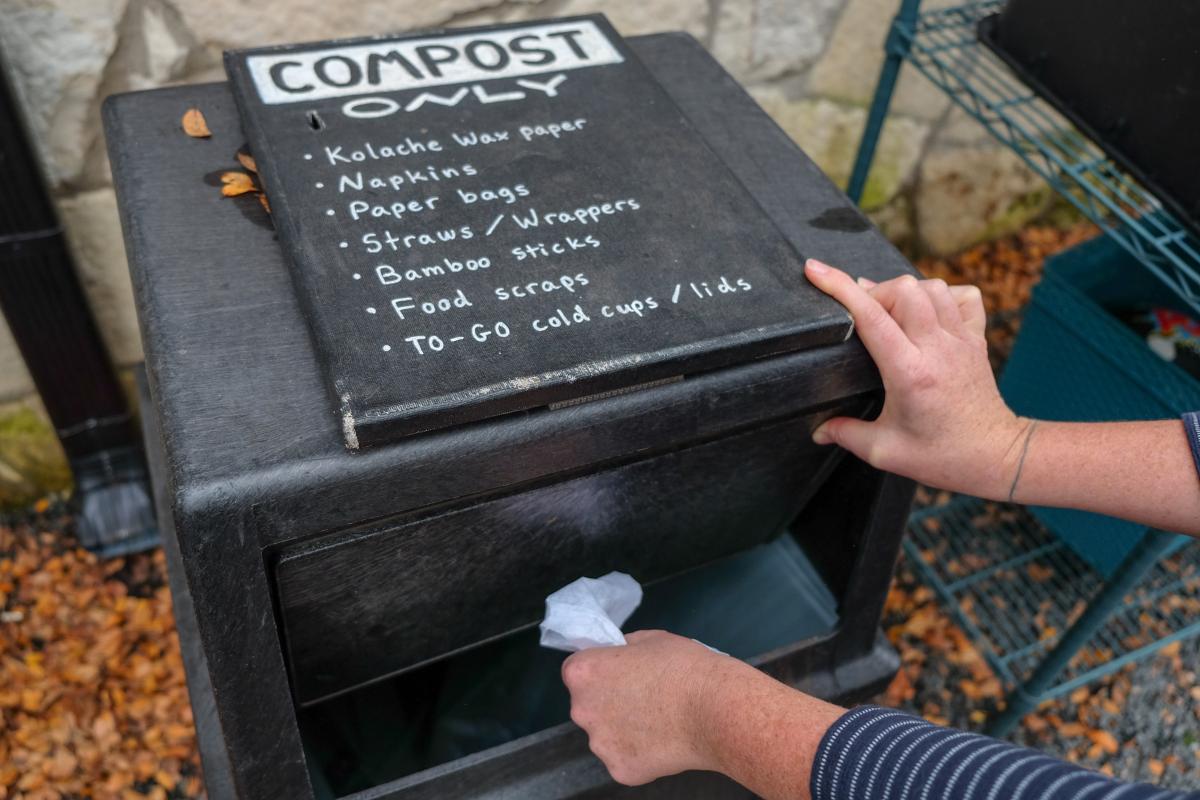 Photo of compost bin and person's hand placing an item in it. Bin reads "Compost only" 