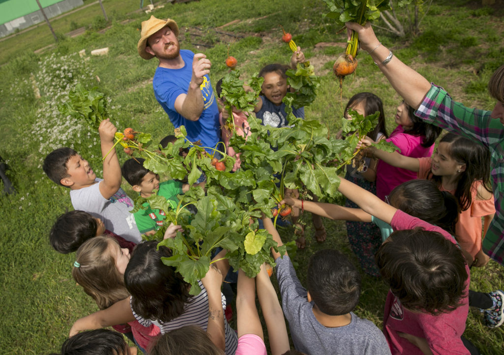 Ilya with a bunch of students standing in a circle holding up radishes they picked from a garden.