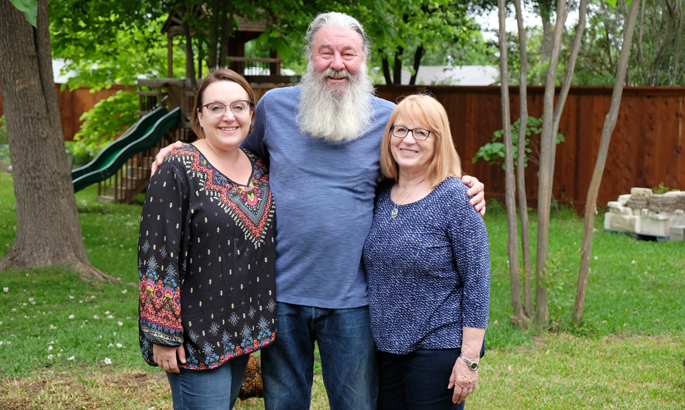 Photo with Jerry, Lauree, and Amy Bramwell standing in front of green grass, trees, and a playscape.