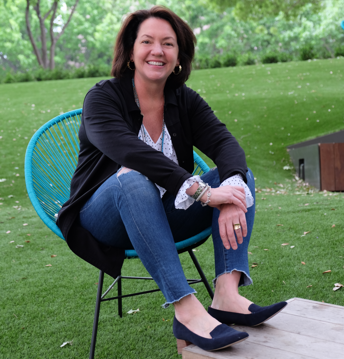 Laura Huffman seated in a teal blue chair with green grass behind her.