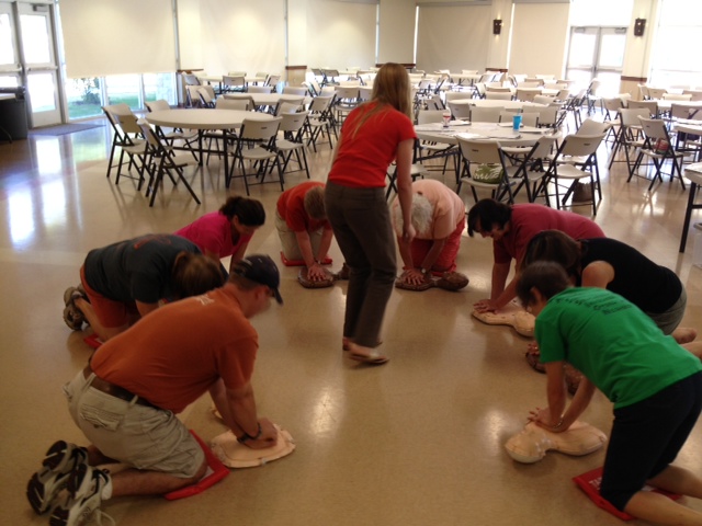 A TAKE10 Trainer giving the TAKE10 class. She is in the middle of the group giving feedback while they are practicing compressions.