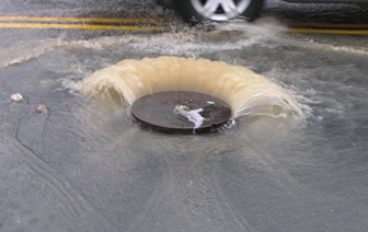 The lid of a sewer being pushed up by the water pressure that built from FOG.