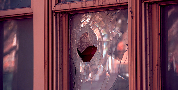 broken glass window with a circular hole on a maroon house, possibly from a baseball