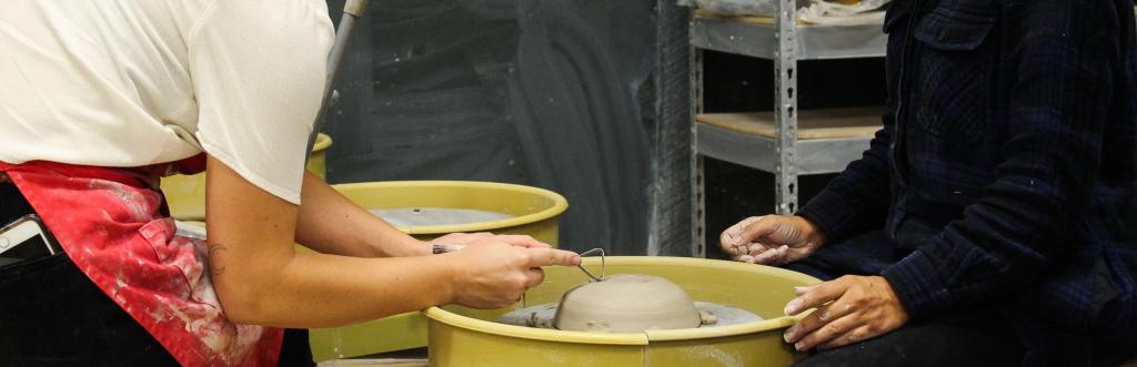 Ceramic arts instructor assists student with wheel throwing exercise