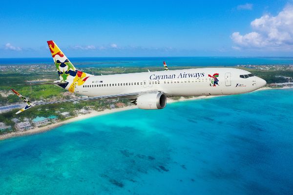 Photo of a Cayman Airways plane flying over the ocean during the day time.