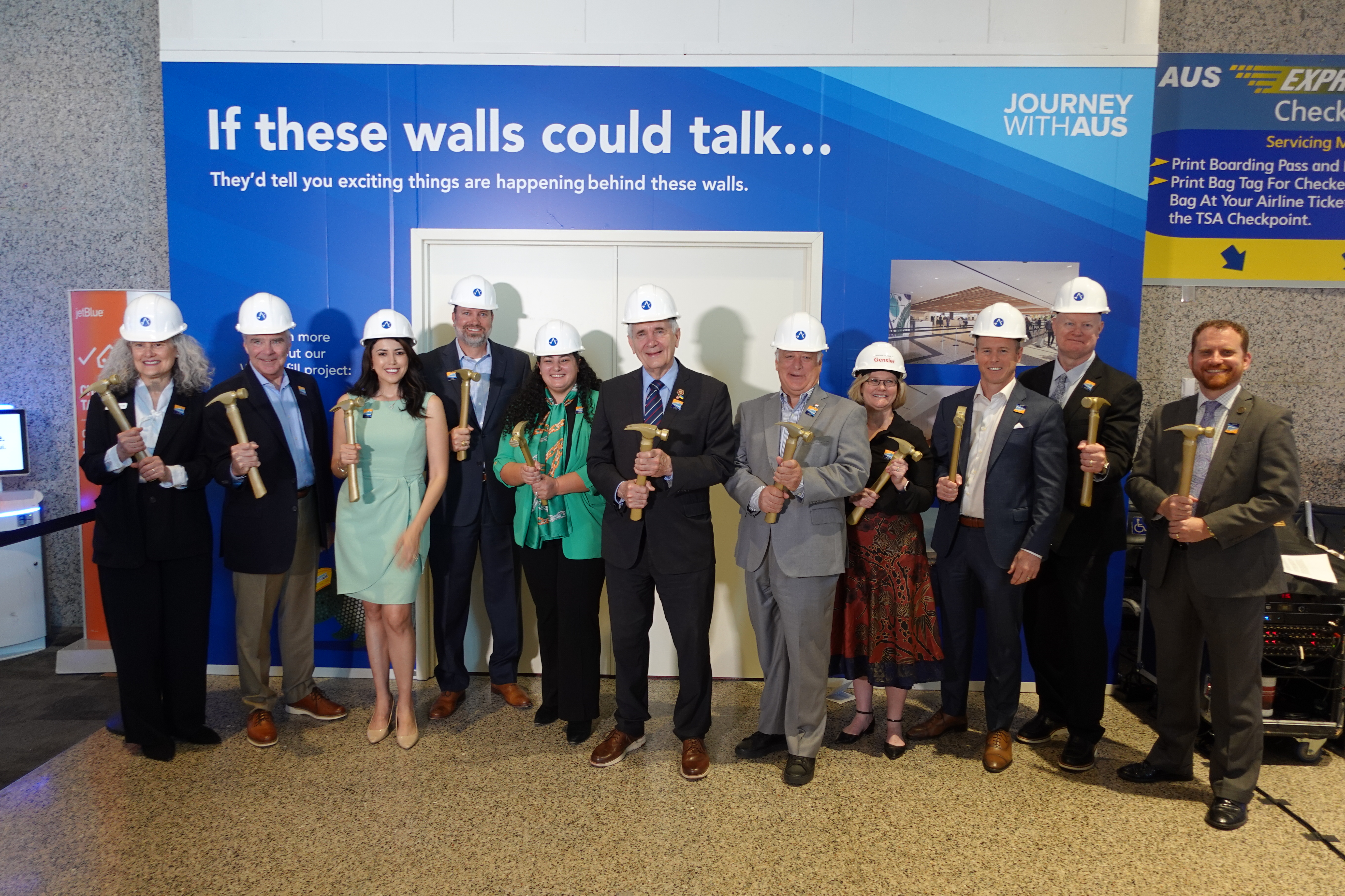 Eleven people standing in front of a construction wall with West Infill and TSA Checkpoint 3 Expansion information shown on the wall. 