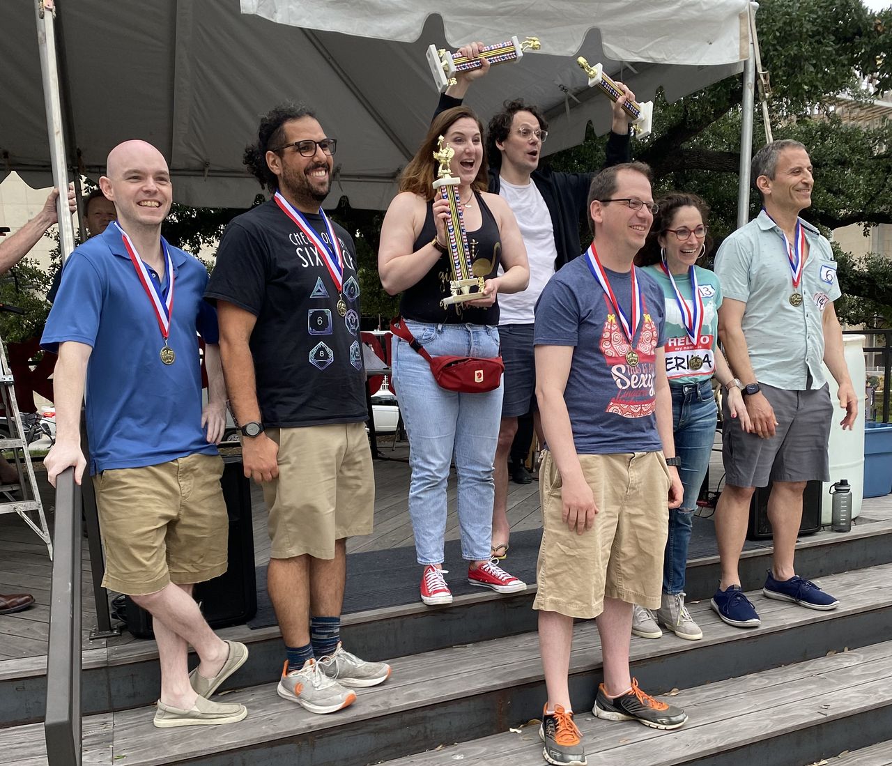 The 7 winners of the Pun-Off, wearing medals and holding trophies.