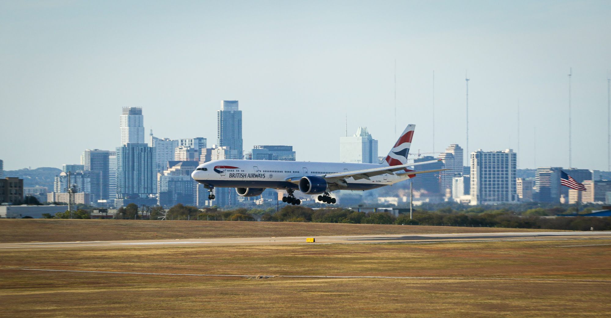 A British Airways 787 Dreamliner lands on a runway at Austin-Bergstrom International Airport. In the background is the Austin city skyline.