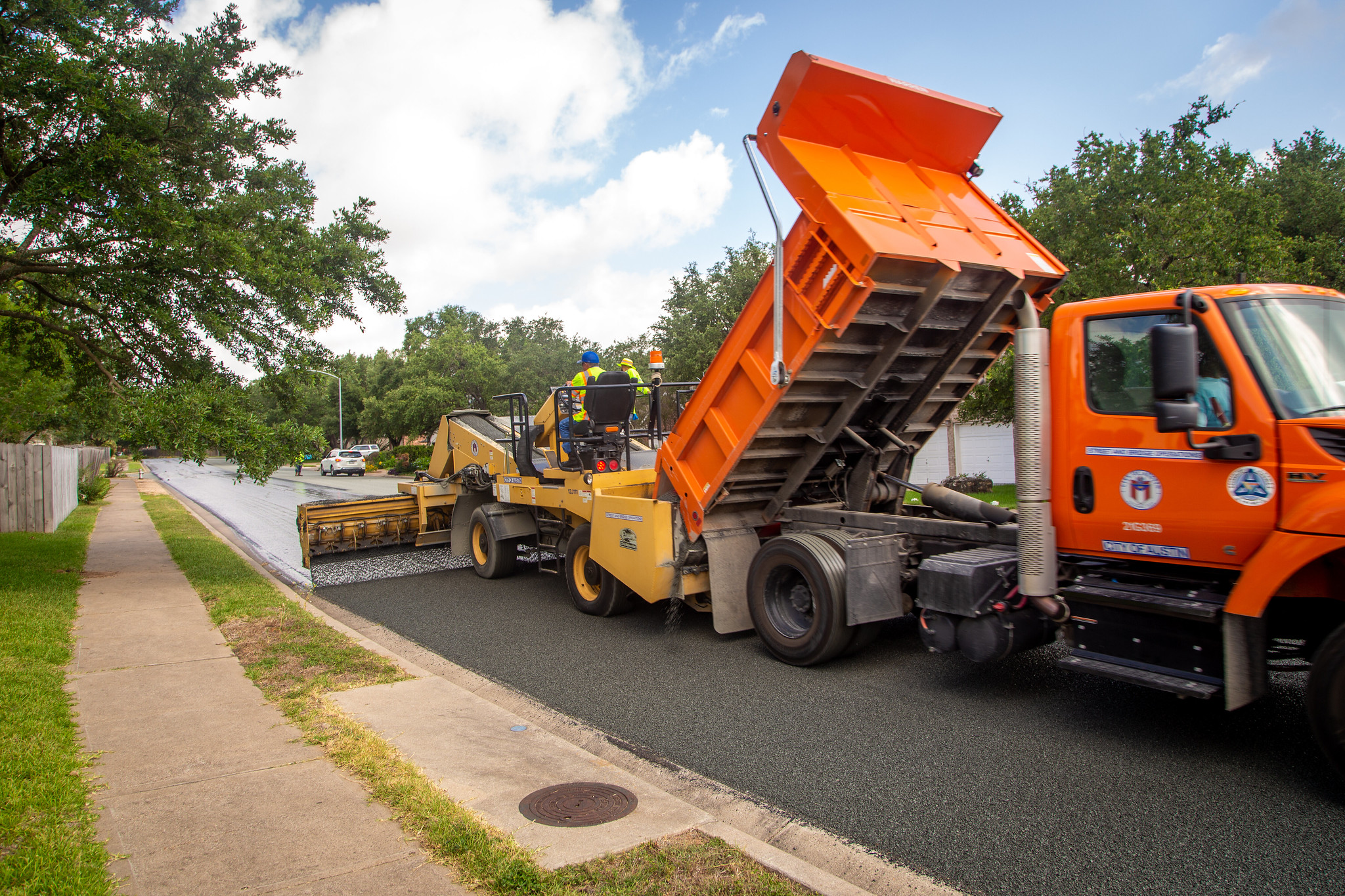 A bright orange truck applying a street resurfacing treatment to a neighborhood street