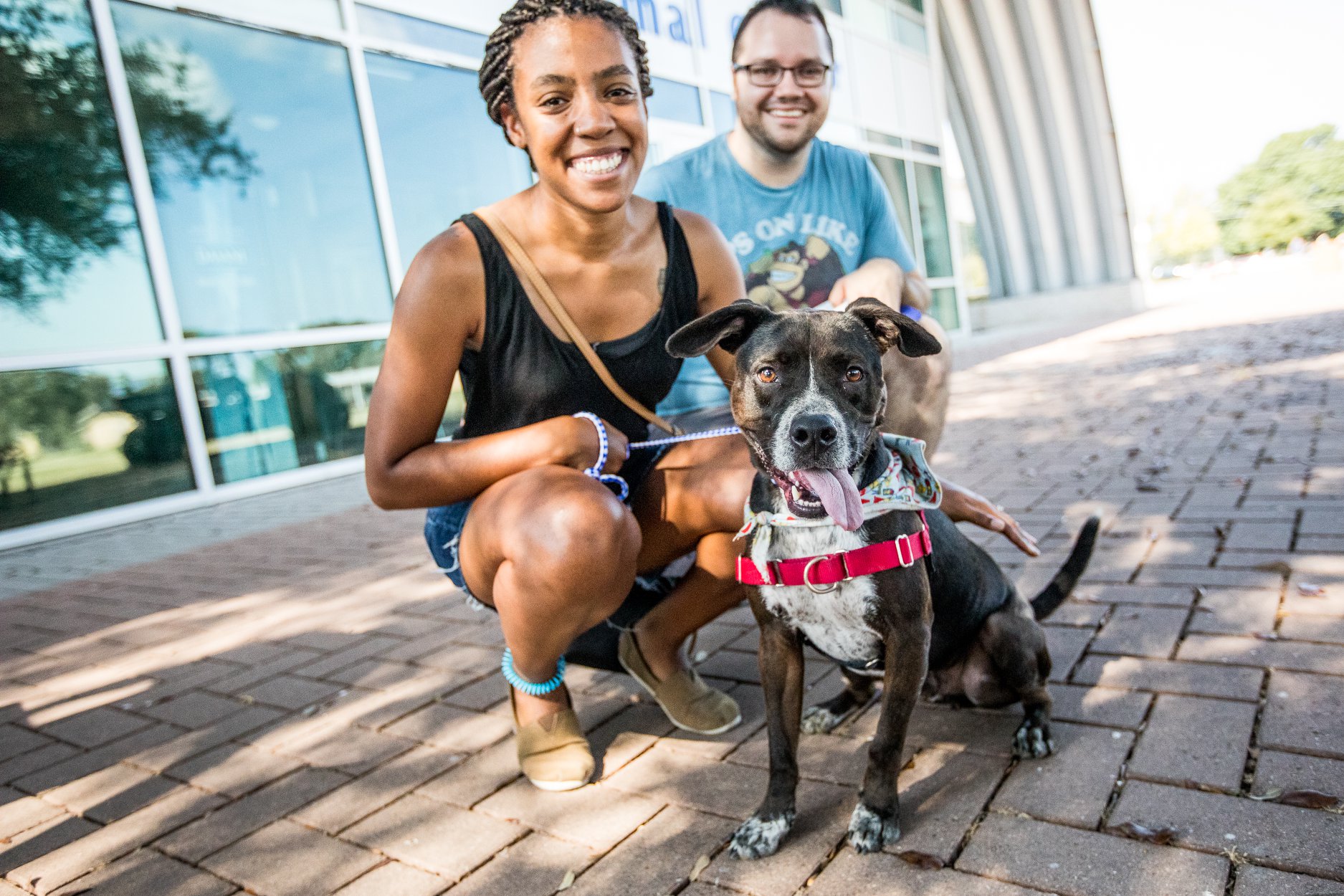 Two people pose with a dog in front of Austin Animal Center