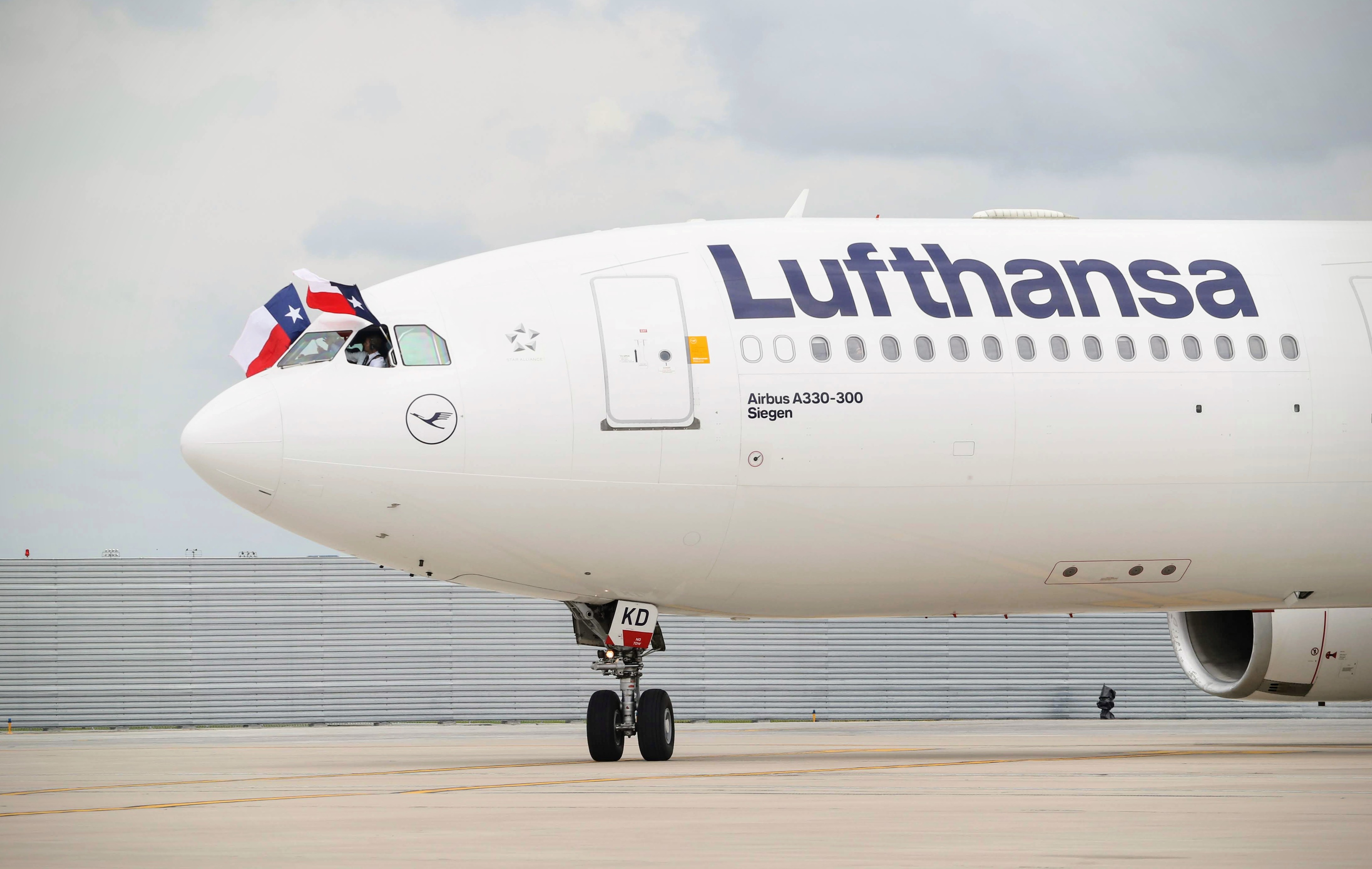 Photo of a Lufthansa airplane on a taxiway. National flags are being held outside of the cockpit of the plane.