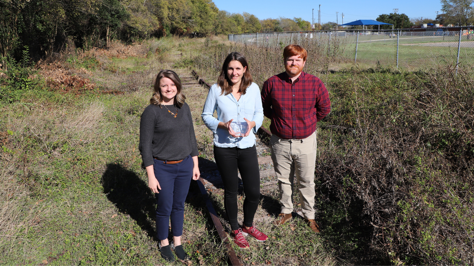 Representatives from the City of Austin Urban Trails Program and CAMPO accept a Planning Achievement Award from the Texas Chapter of the American Planning Association. Photo of three people standing on a lawn and smiling. One person holds a glass award.