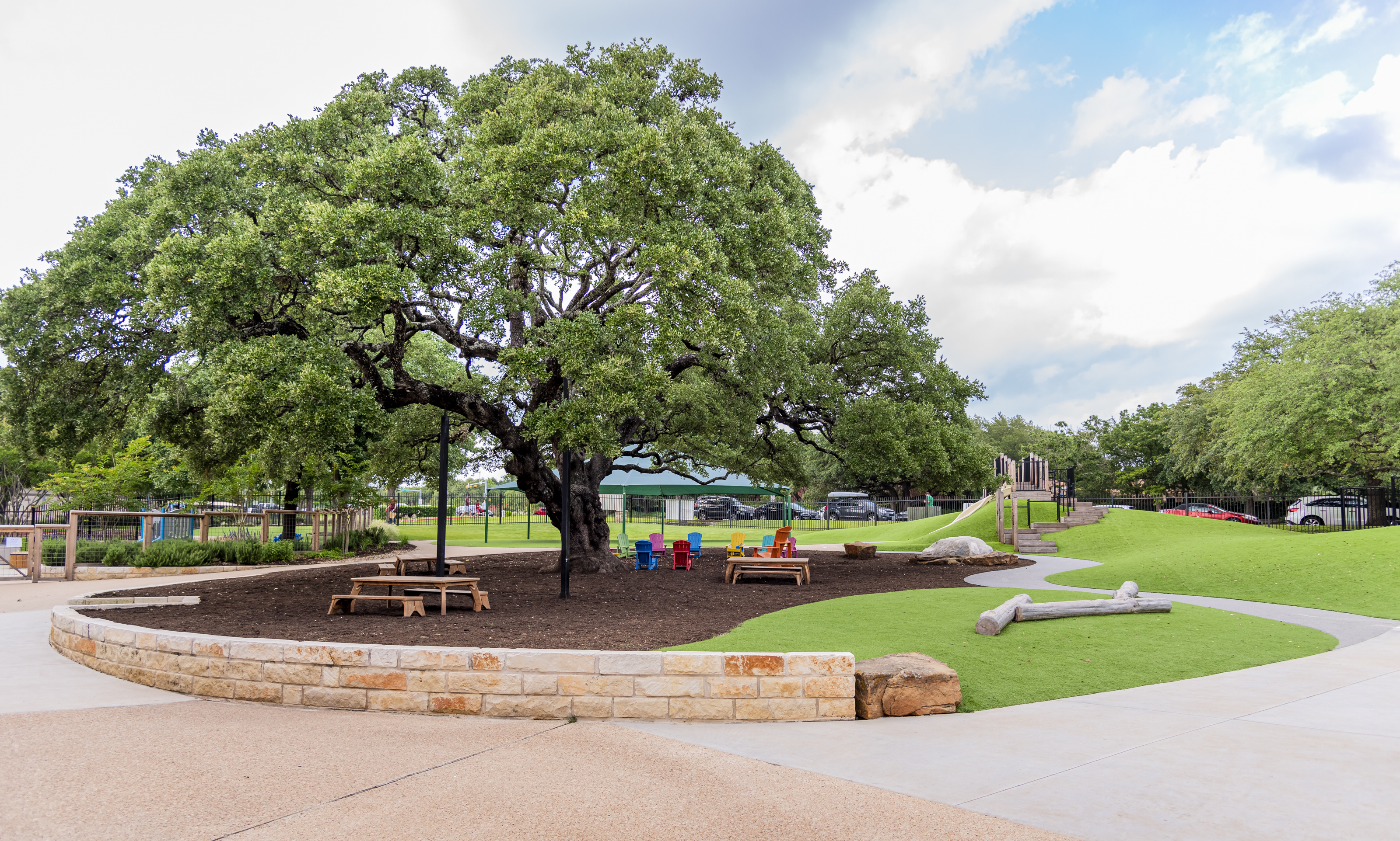 a large oak tree with picnic tables and a playscape