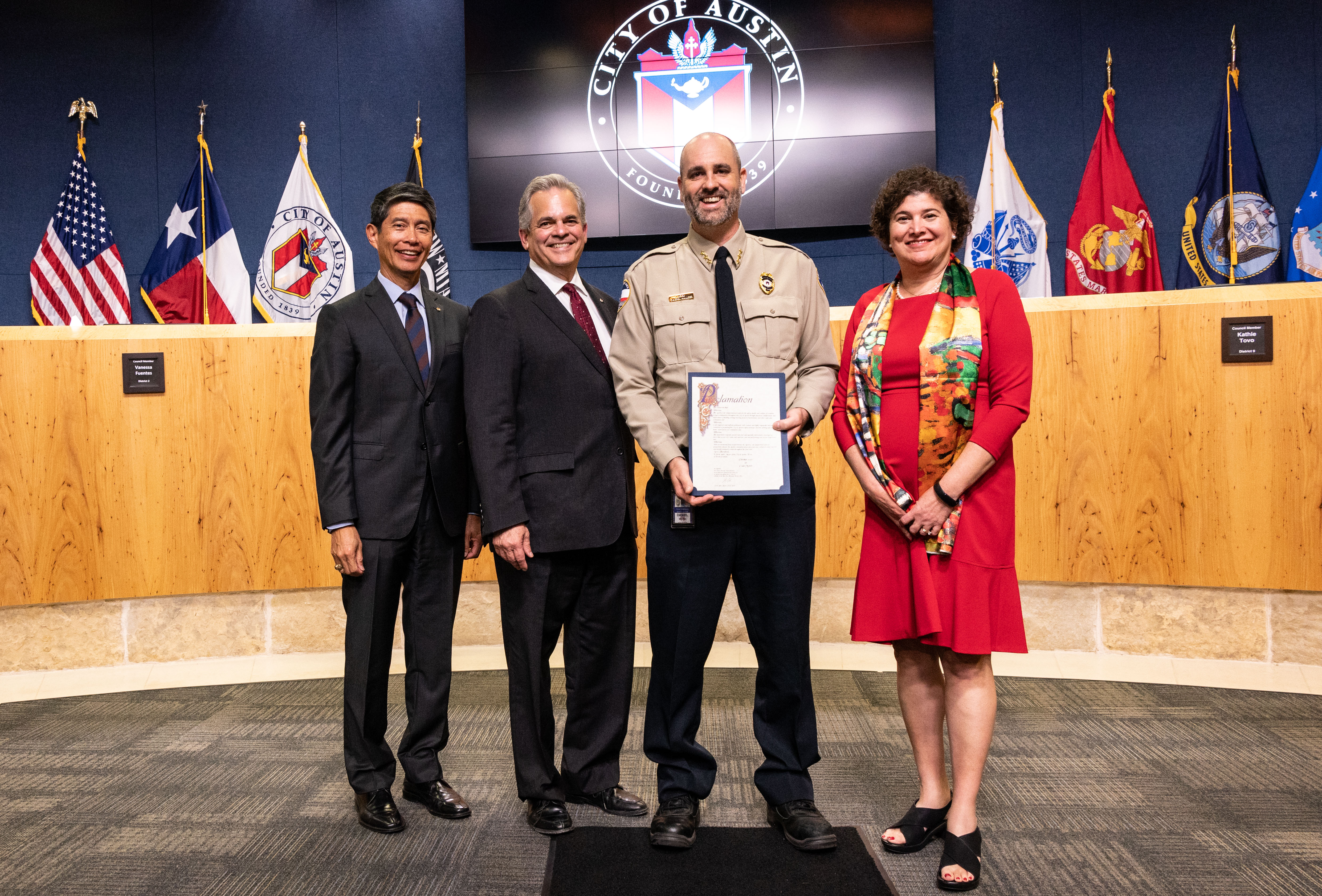 Assistant Director Daniel Word accepts the Proclamation of October as National Code Compliance Month. In City hall with the City logo and the City Councilmember benches in the background, Code Assistant Director Daniel Word poses with City proclamation of Code Month in his hands with Assistant City Manager Rey Arrellano and City Mayor Steve Adler to his left and Mayor Pro-Tem Alison Alter to his right.