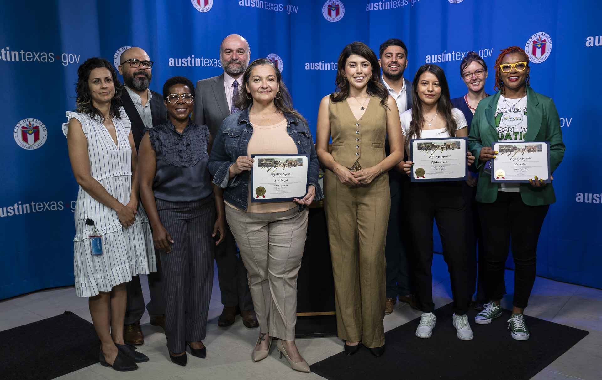 Image shows several Navigators holding certificates in recognition of their community efforts. They are standing with Housing staff and City Council members in front of a blue background with the City of Austin logo and website.