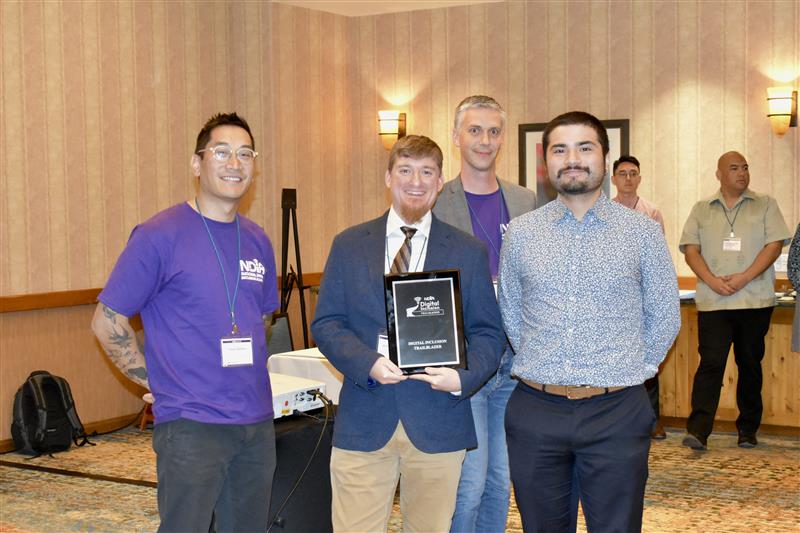 photograph of four men, one of them is holding an award that says Digital Inclusion Trailblazer