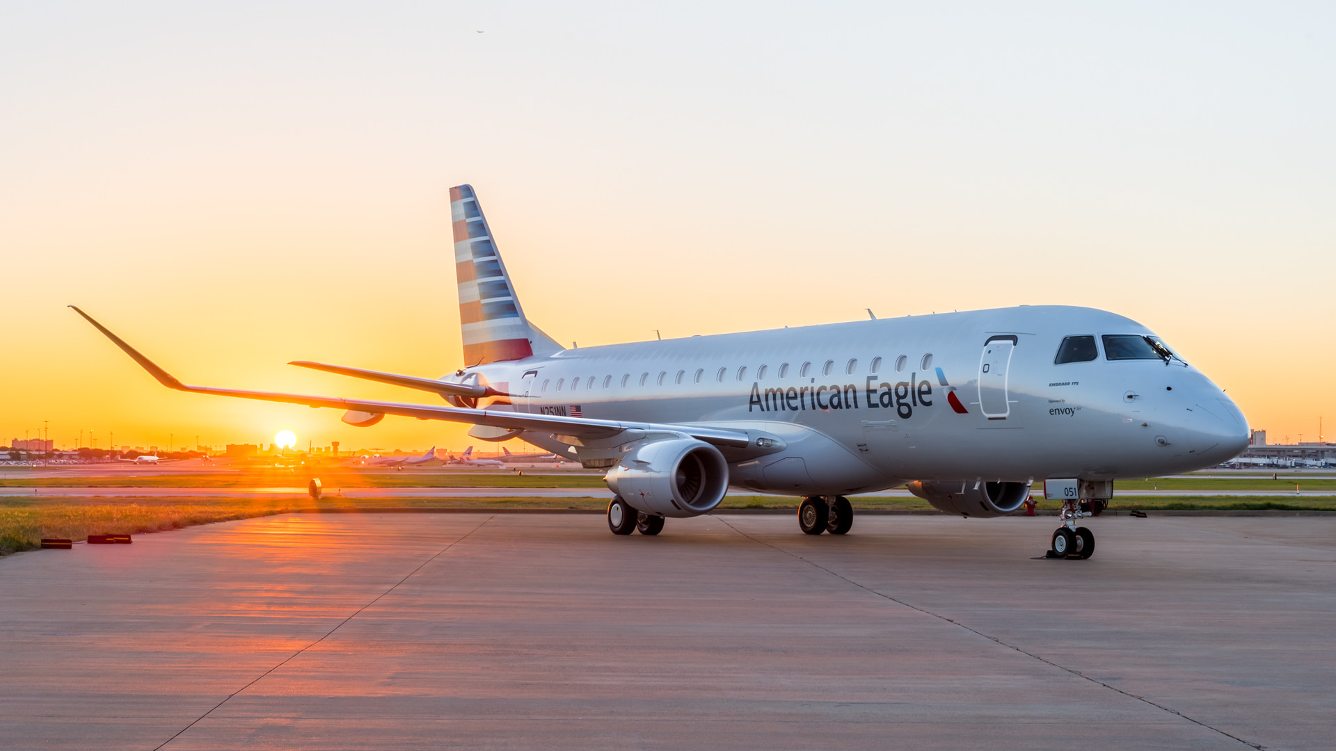 An American Airlines Embraer 175 aircraft sits on the tarmac in front of a beautiful orange sun rise