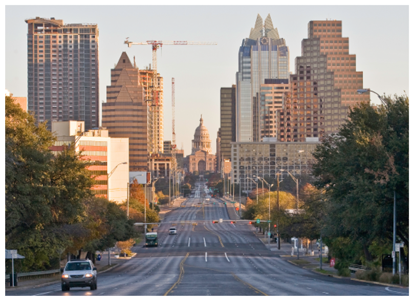 a street view photo of Downtown Austin with the Capital directly in the center of the photo with tall, sun kissed buildings to the left and right