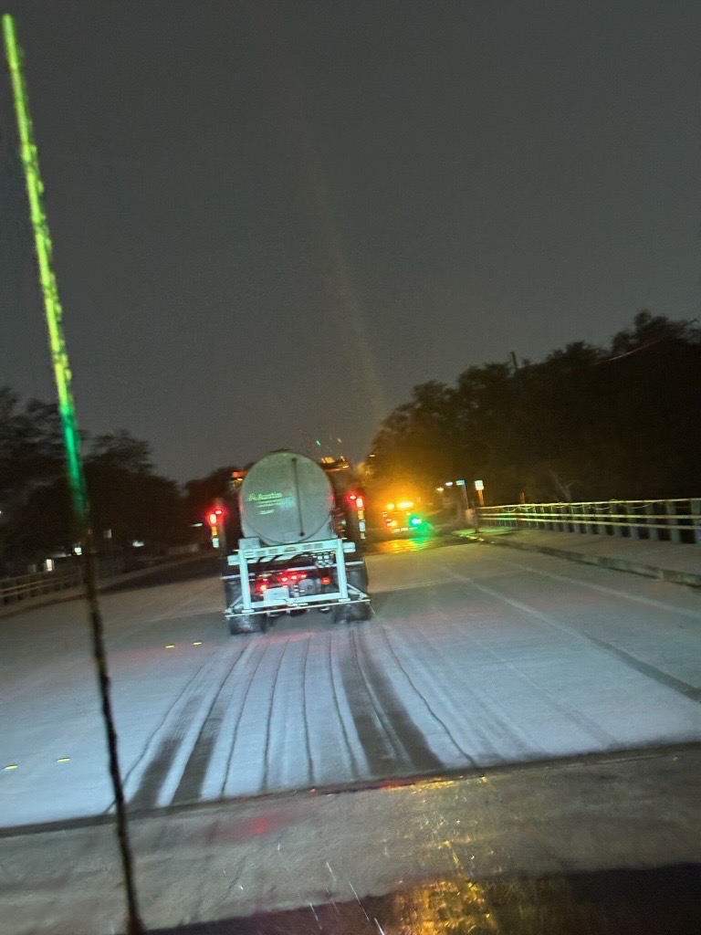 photo of ice on the street with a truck spreading de-icing brine in the foreground.