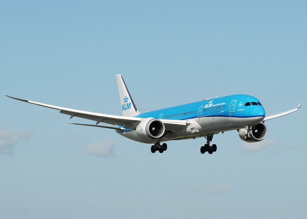 A KLM dreamliner is bright blue and flies in the sky