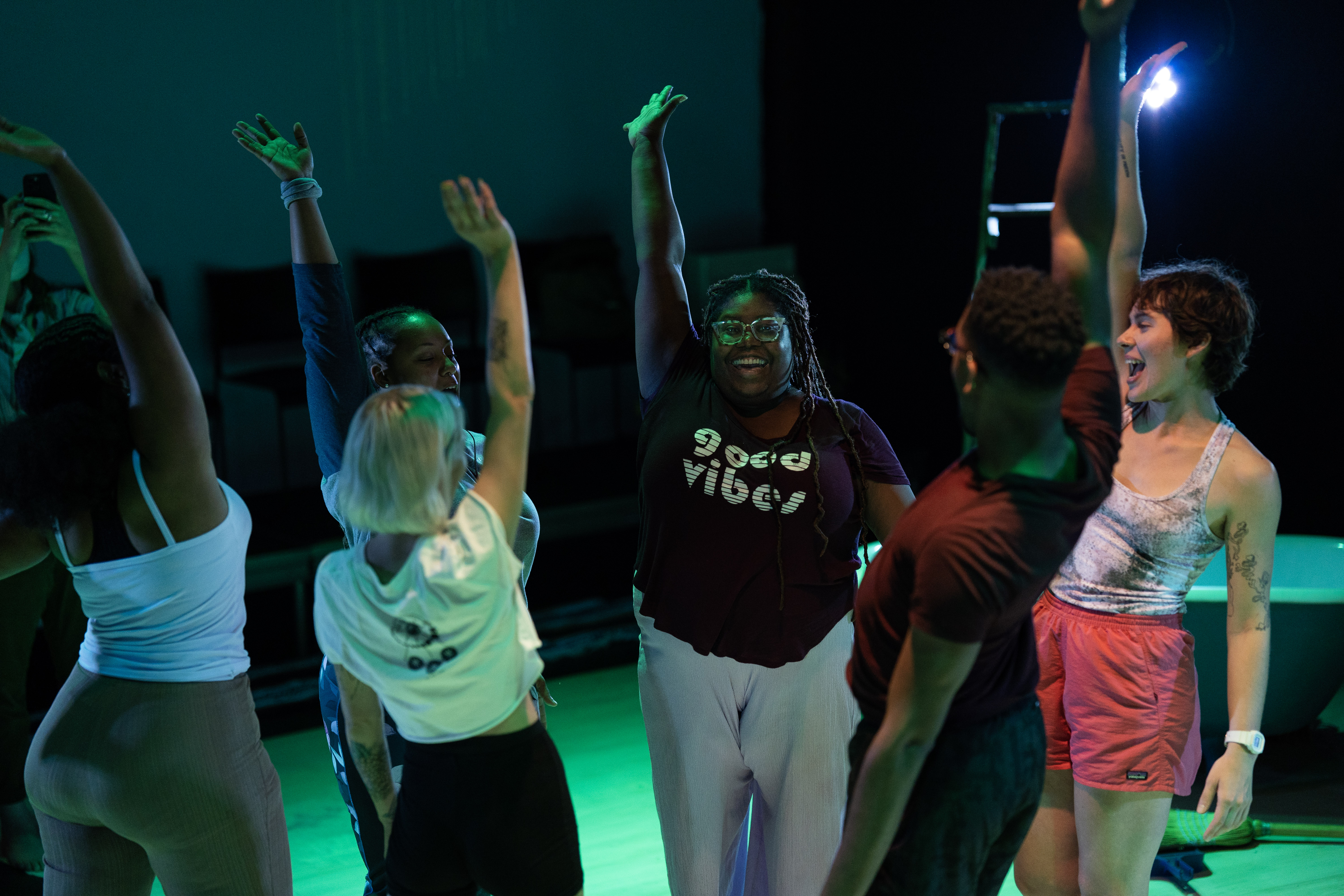 Thrive Grant Opens A group of people on stage standing in a circle raising their arms in excitement.