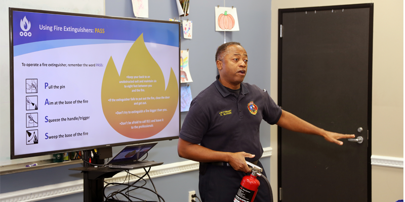 A photo showing an Austin firefighter demonstrating how to use a fire extinguisher at a classroom training for the community.