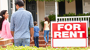 Family looking at a house with a For Rent sign in the yard