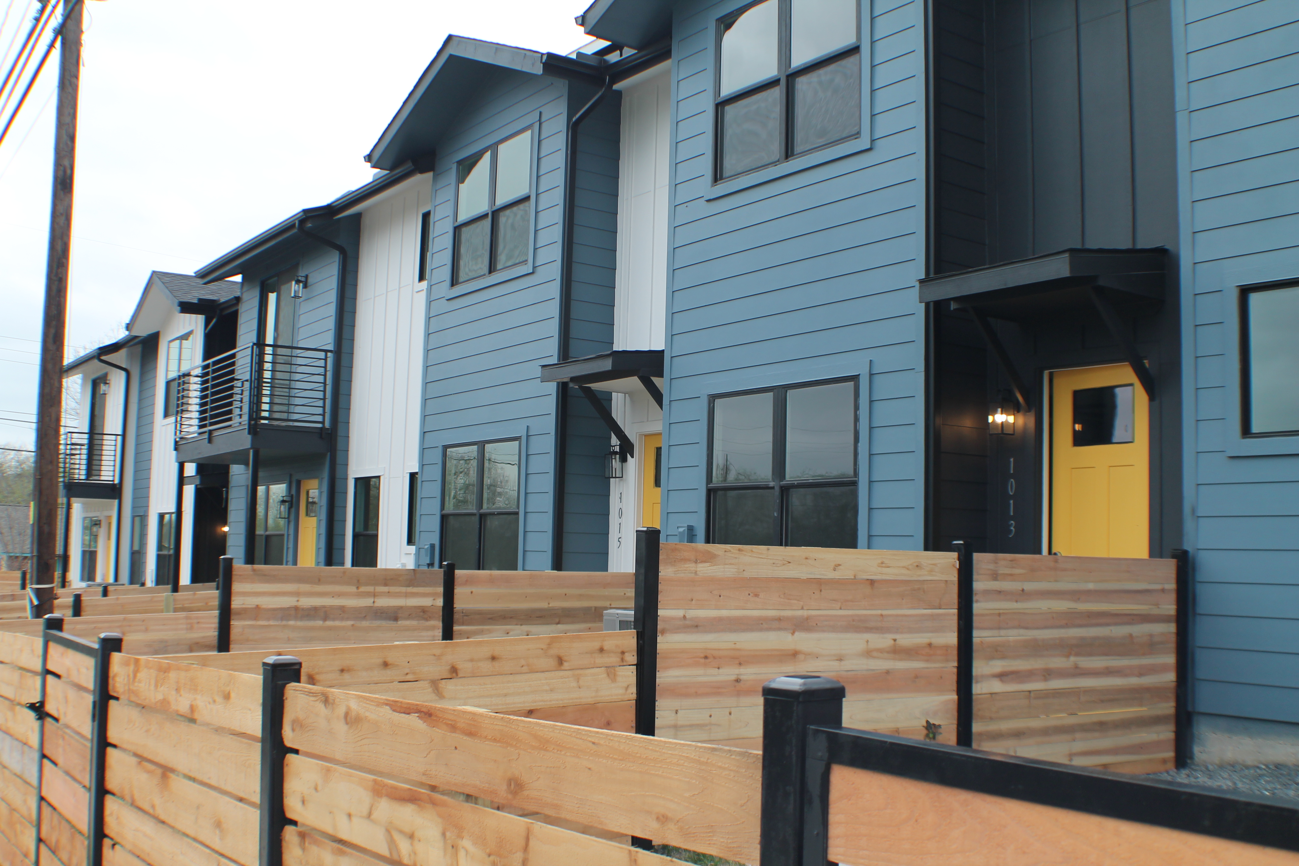 Row of blue and white townhomes with bright yellow doors and individually fenced yards