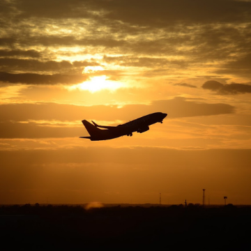 Photo of a plane taking off with and orange sunset in the background.