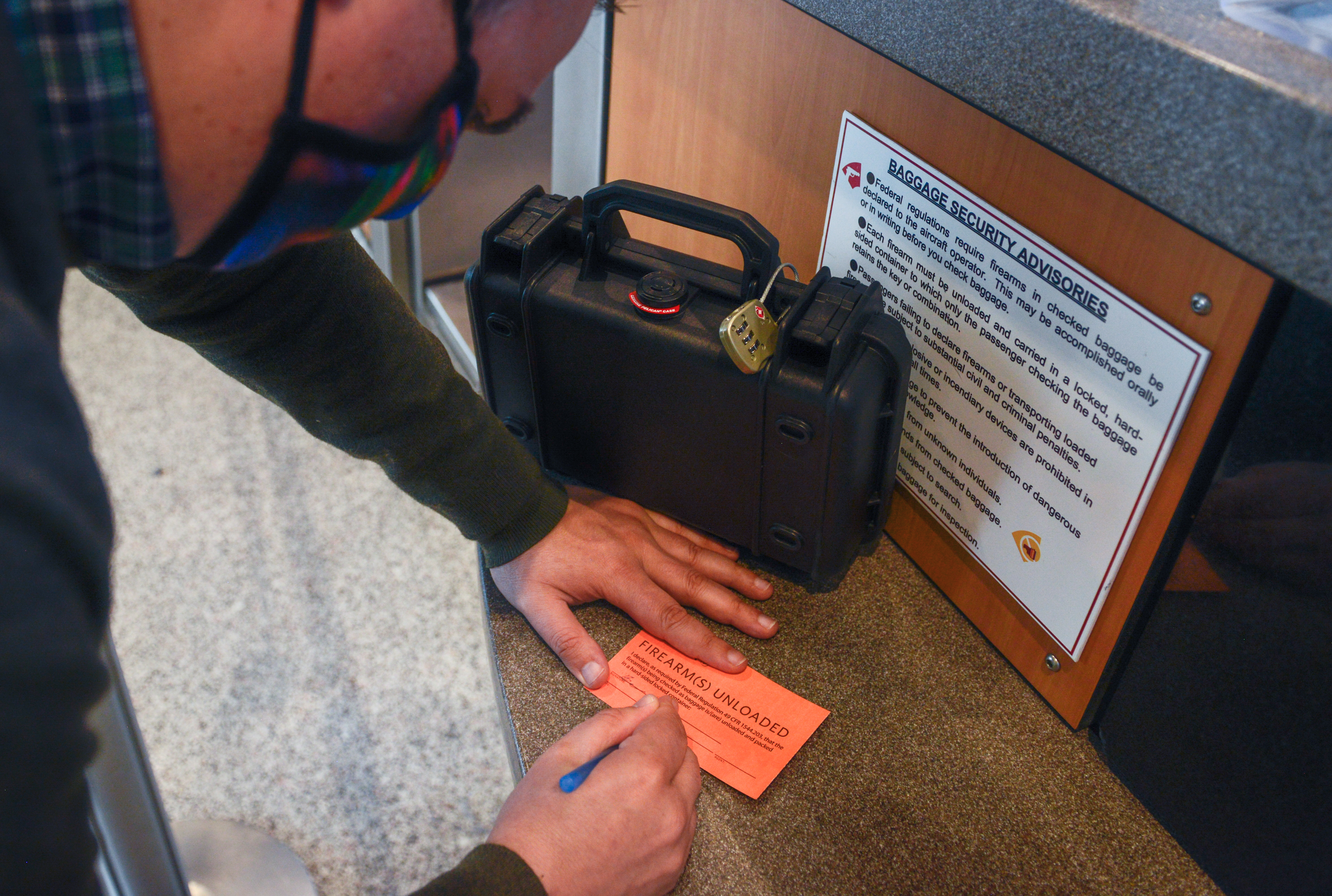 Photo of a man at an airline ticket counter in Austin-Bergstrom International Airport filling out a declarations page for his firearm. A hard-sided and locked firearm case is located next to him.