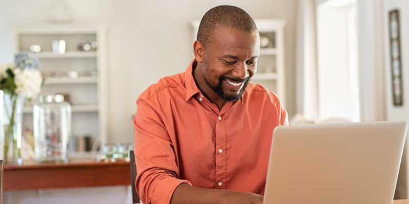 Man smiling while typing on a laptop