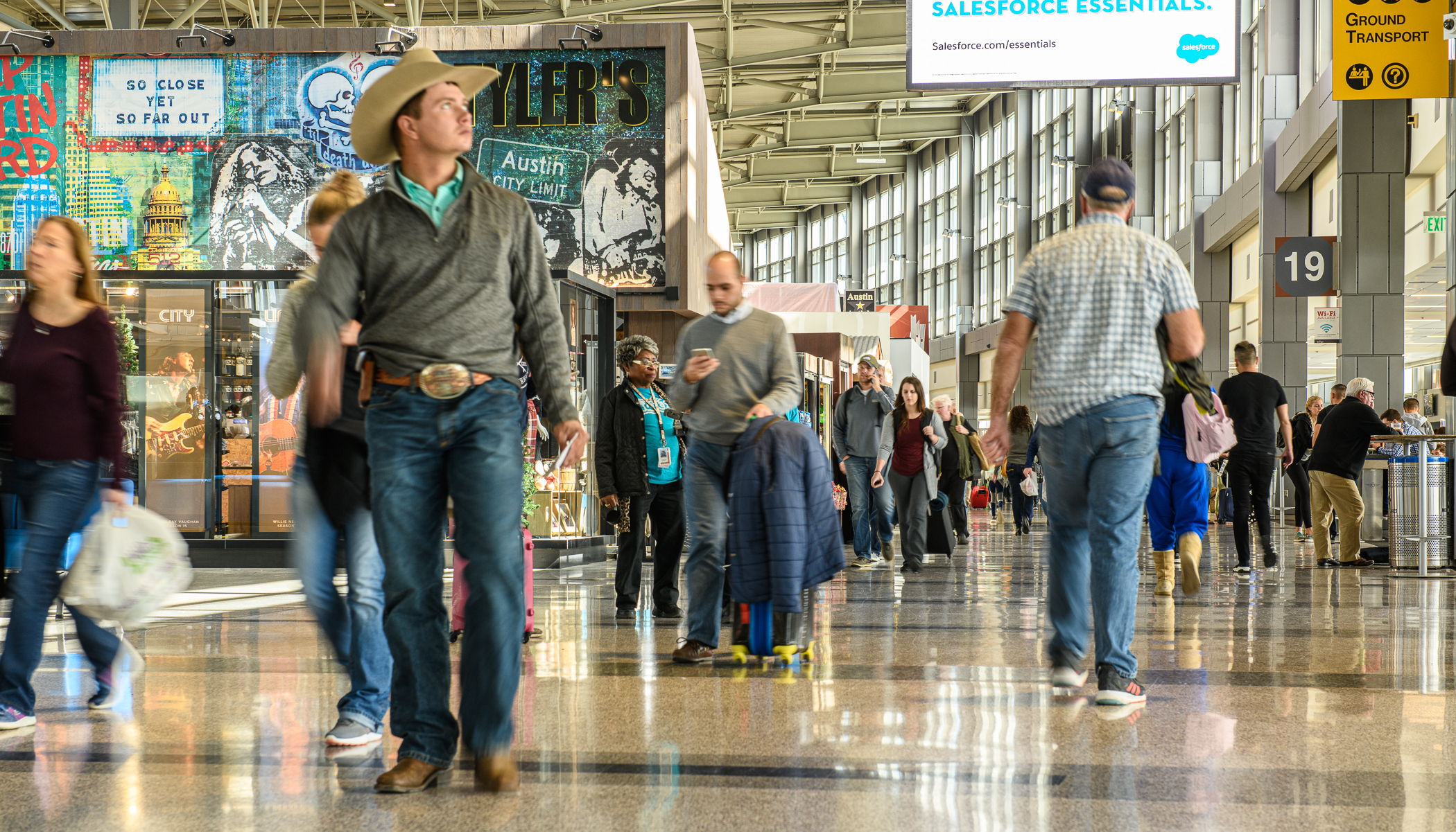 Man dressed in western wear and cowboy hat walking in a busy airport termina.