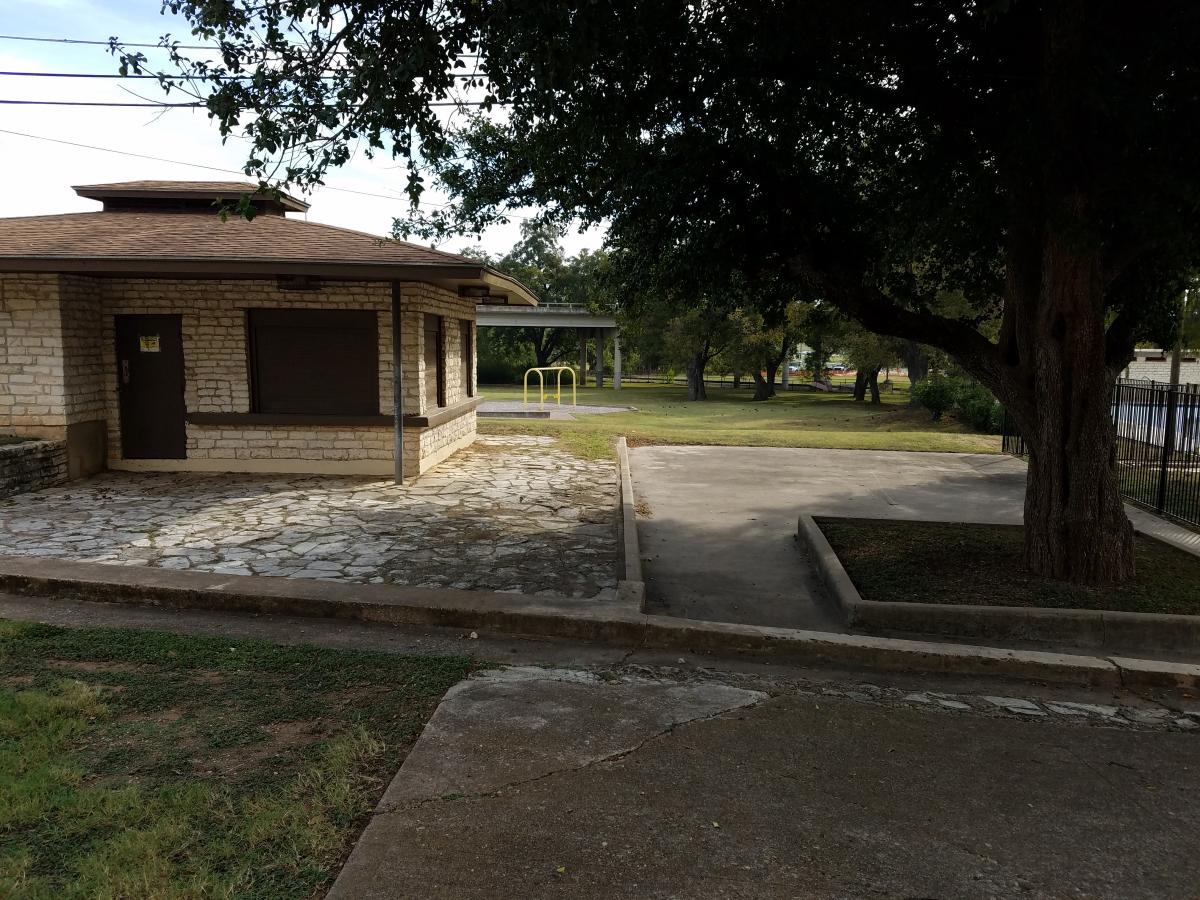 Existing site showing current stone structure and sidewalks with curbs next to large trees.
