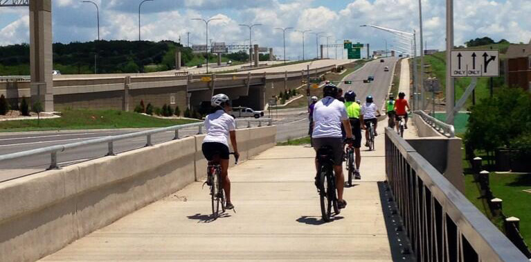  A group of people bicycling on a shared use path along US 290.