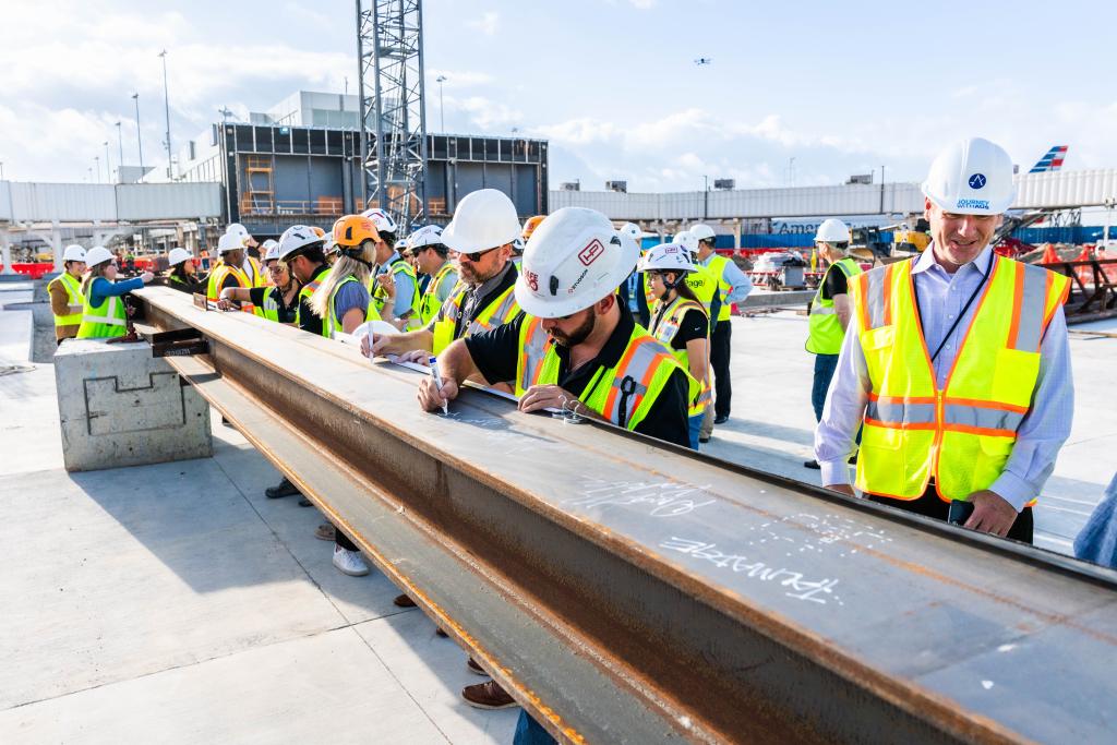 Project team members wear safety vests and hard hats while they sign a steel beam