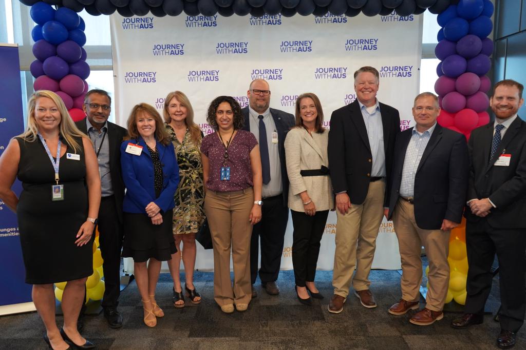Airport project team photo under colorful balloon arch in front of Journey With AUS banner.