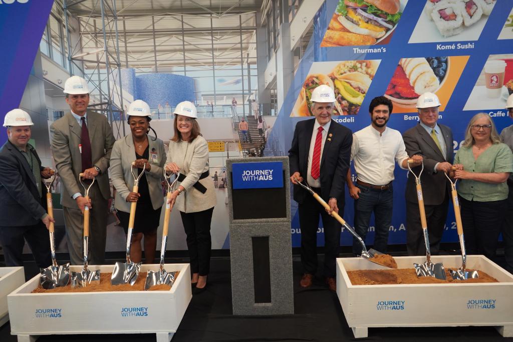 Guest speakers and VIP's wearing white hard hats and shovels to ceremonially turn dirt. 