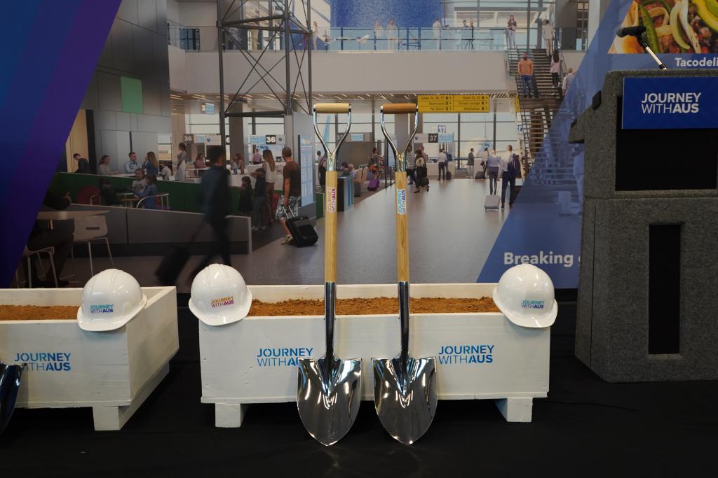 White boxes filled with dirt with Journey With AUS logo pictured with white hard hats and shiny silver shovels.